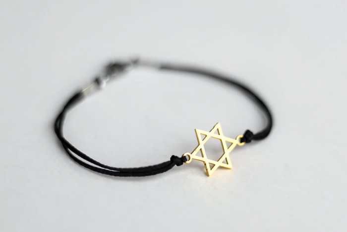 Black bracelet with a gold Star of David charm on a light gray background