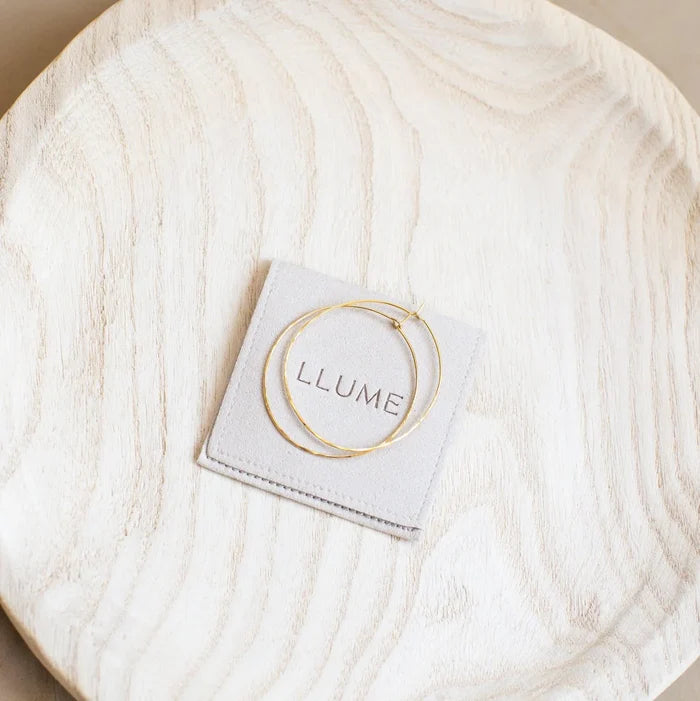 The Summer Shine Set by LLUME Jewelry features thin gold hoop earrings, perfect for summer stacking, displayed on a light gray LLUME card atop a round, light wooden plate with a natural grain pattern.