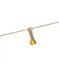The Sunspill Necklace by LLUME Jewelry showcases a delicate gold multi-length chain with a yellow teardrop-shaped gemstone pendant, accented by small clear stones set above it, and is displayed against a white background.