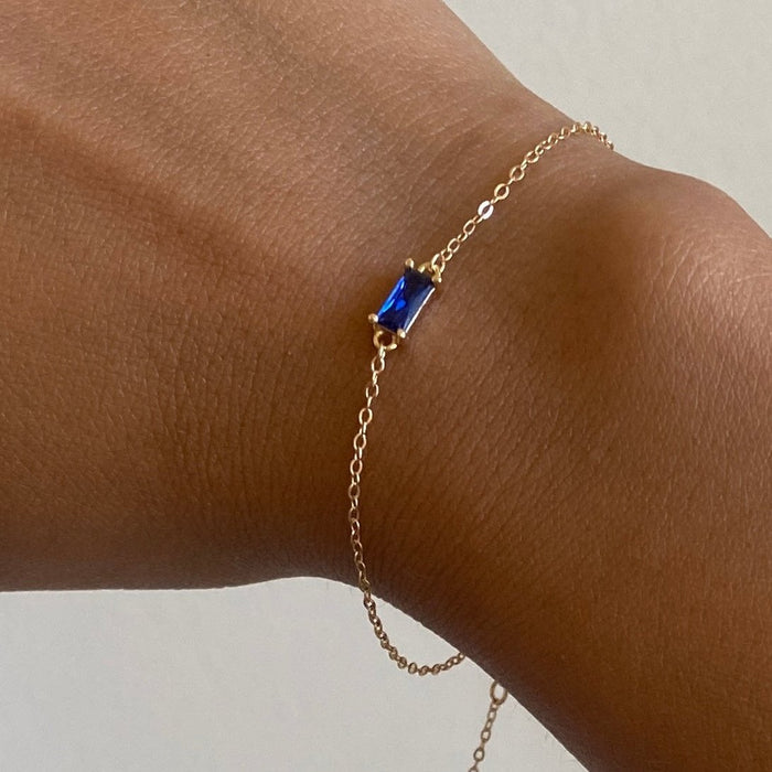 The Taylor Bracelet by LLUME Jewelry showcases a rectangular sapphire blue gemstone on a gold plated sterling silver adjustable chain, elegantly displayed on a wrist against a plain light background.