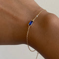 The Taylor Bracelet by LLUME Jewelry showcases a rectangular sapphire blue gemstone on a gold plated sterling silver adjustable chain, elegantly displayed on a wrist against a plain light background.