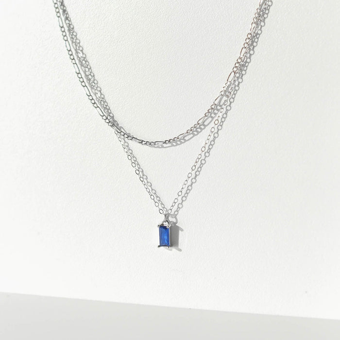 The Taylor Daily Set Silver by LLUME Jewelry features a double-layered silver necklace with a small blue rectangle gemstone pendant on the shorter chain, showcased against a plain white background.