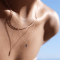 A woman's neck and shoulders are shown in sunlight, wearing the LLUME Jewelry Taylor Daily Set—featuring a delicate necklace and small rectangular Taylor Pendant—with a clear blue sky in the background.