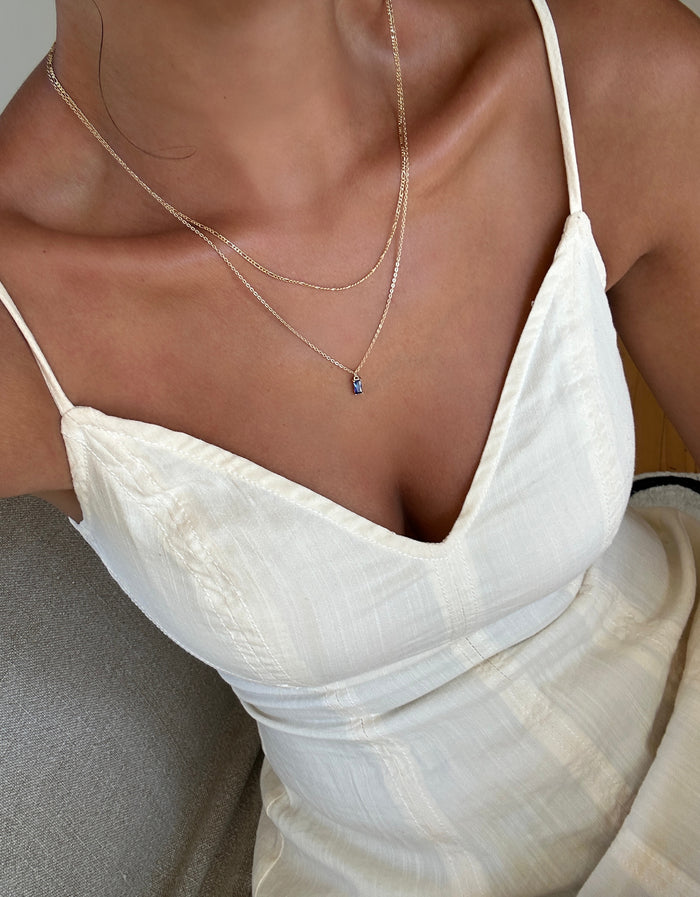 A person wears a cream, sleeveless dress with thin straps and a deep neckline, accessorized with the LLUME Jewelry Taylor Daily Set. The image is cropped to display the upper torso and part of the dress.