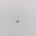 The Taylor Huggies by LLUME Jewelry are small gold-plated earrings with round blue stones, shown on a plain light gray background.