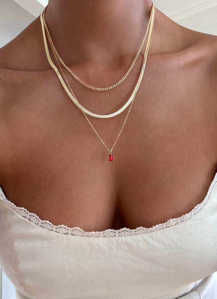 A woman in a white lace-trimmed top wears the LLUME Jewelry Tomato Girl Set—three gold layering necklaces, one with a small red pendant—visible from shoulders to chest.