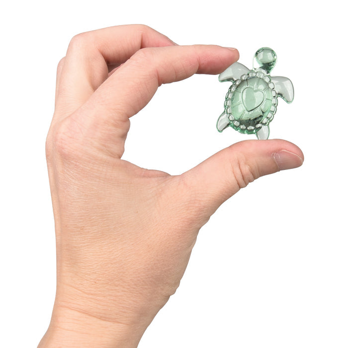 Hand holding a small green turtle figurine with a heart on a white background