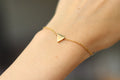 A gold-tone stainless steel chain bracelet with a tiny triangle bead charm, being worn on a person's wrist.