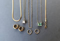 The Vacation Capsule Set by LLUME Jewelry features gold chains with distinctive pendants and chic gold earrings, elegantly displayed on a gray background—your go-to summer jewelry collection.