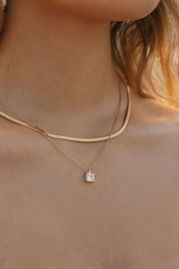 A close-up of a woman’s neck wearing LLUME Jewelry’s Vacation Capsule Set: one sleek chain and one delicate chain with a square stone pendant—perfect for stacking and elevating any jewelry look.