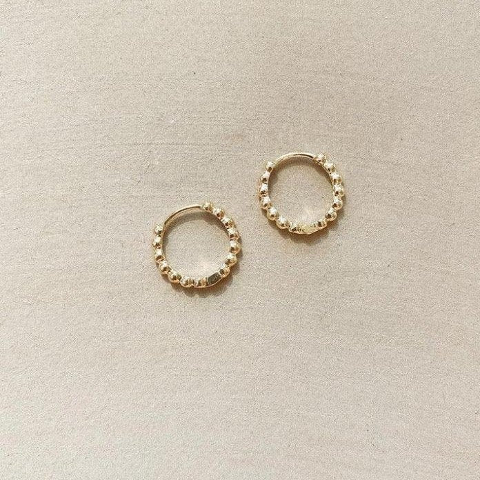 The Summer Shine Set by LLUME Jewelry features two small, gold beaded hoop earrings with a textured finish—perfect summer stackers and one of our best sellers, displayed on a light beige surface.