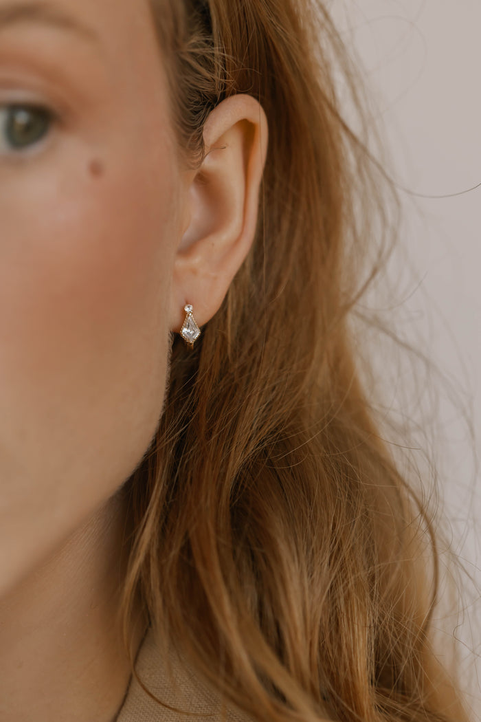 Close-up of a woman's ear with long light brown hair, wearing LLUME Jewelry's Vivian Hoops—small, silver hoop earrings. The side of her face and part of her green eye highlight this elegant accessory.