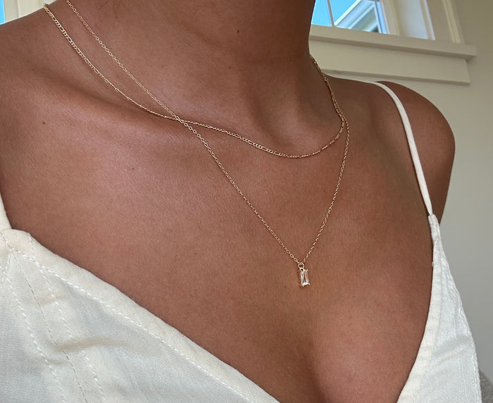 A person wears LLUME Jewelry's Whisper Daily Set with a white V-neck top as sunlight streams in from a window in the background.