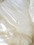 The LLUME Jewelry Whisper Necklace, featuring a delicate gold plated rectangular pendant, is displayed on soft white textured fabric in natural light.