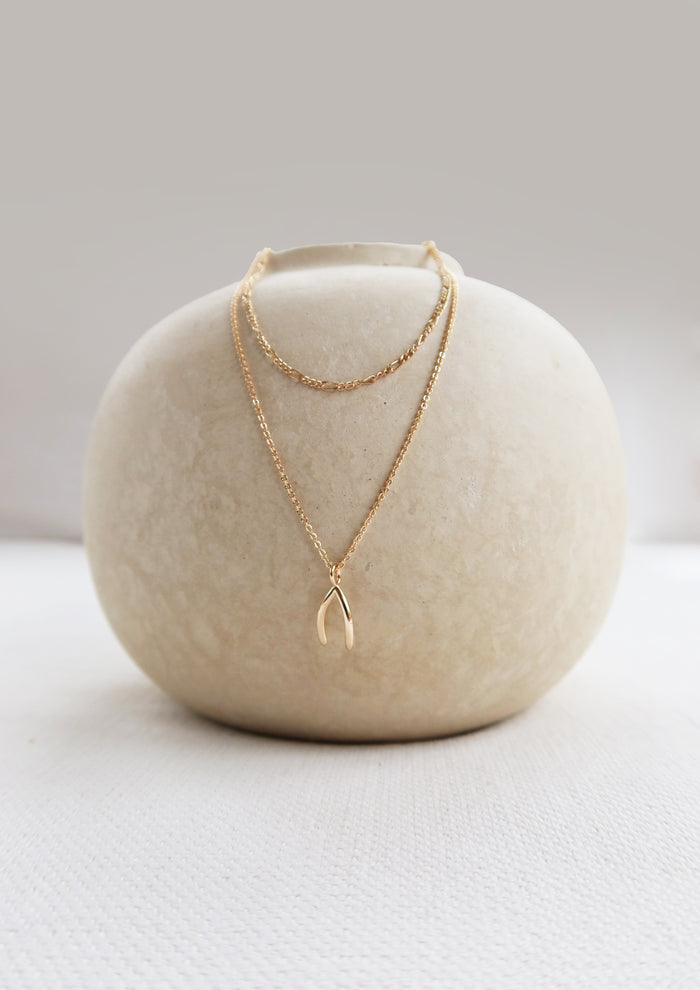 A round, off-white ceramic vase displays the LLUME Jewelry Wishbone Daily Set—featuring the Colette Necklace and Wishbone Necklace—elegantly arranged against a neutral background.